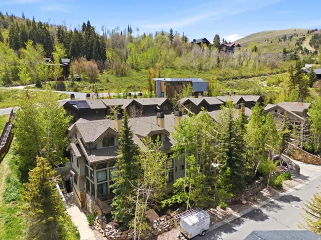 Luxury mountain estate nestled among mature evergreens and aspens, featuring multiple stone and timber-clad residences with peaked rooflines, expansive grounds with natural landscaping, and panoramic views of forested hillsides and rolling terrain
