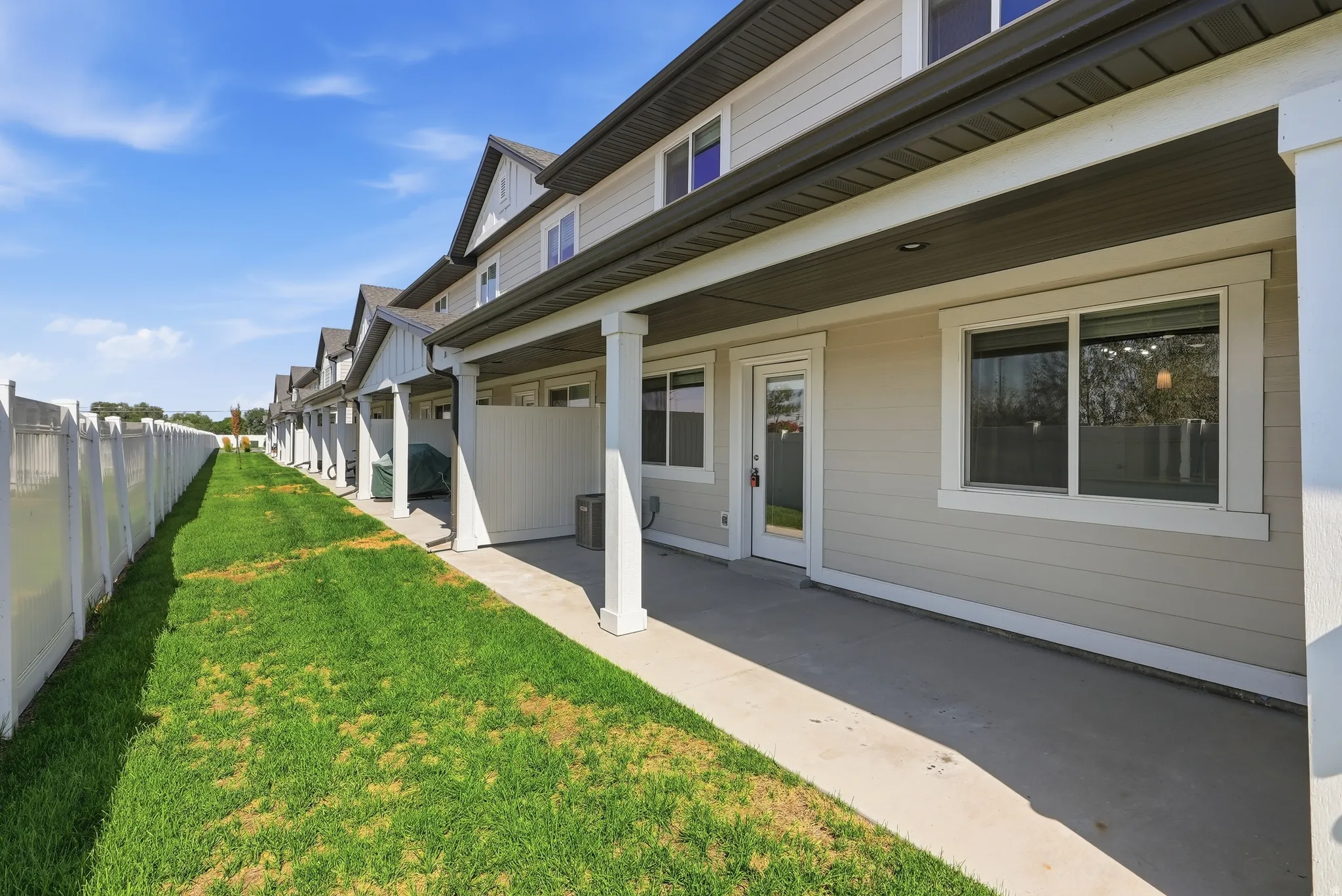 Expansive lawn area, concrete patio, white vinyl fencing, covered patio, and neutral-toned siding