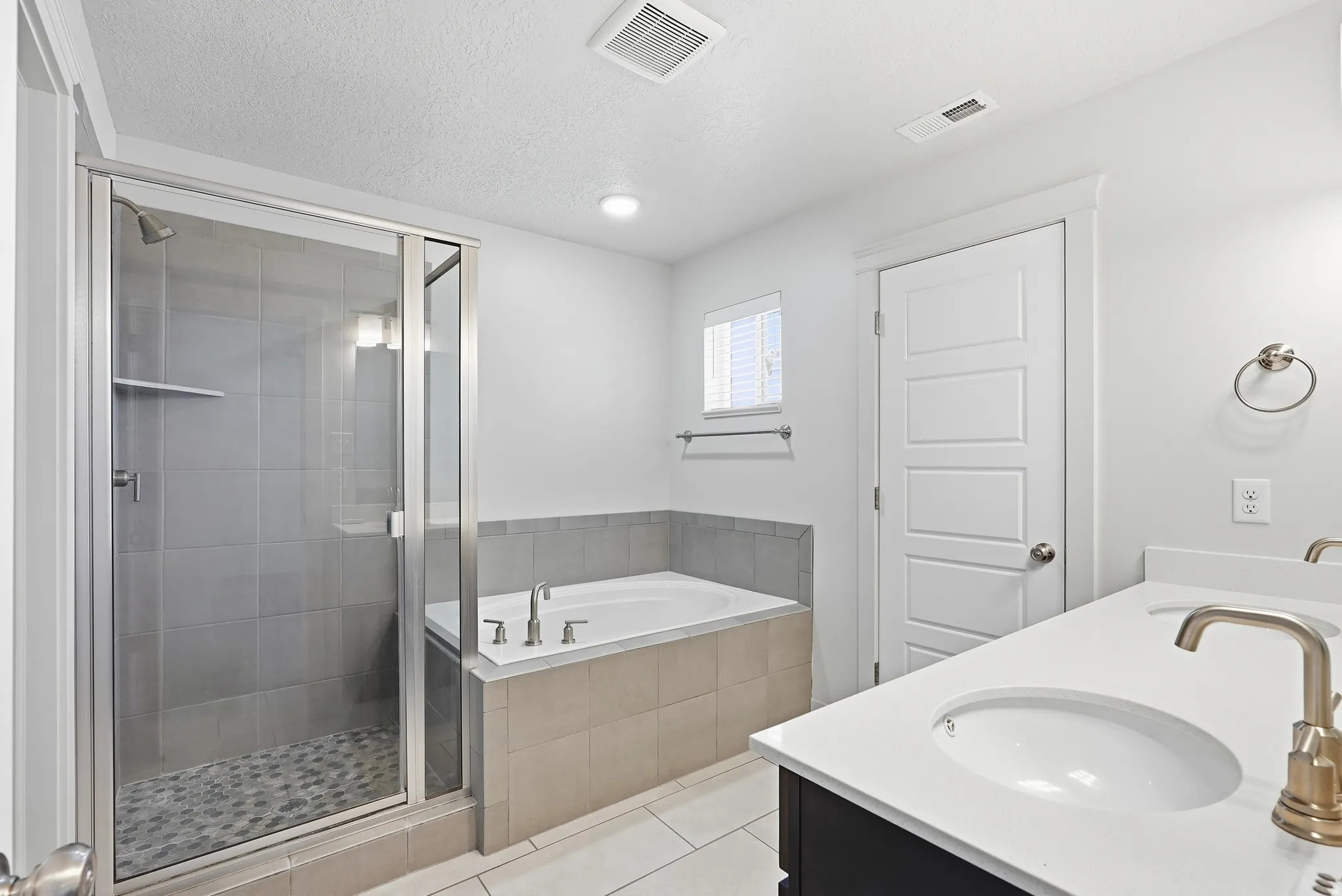Glass-enclosed shower with pebble-tile flooring, built-in soaking tub, dual vanity with undermount sinks, and gold-finish faucets