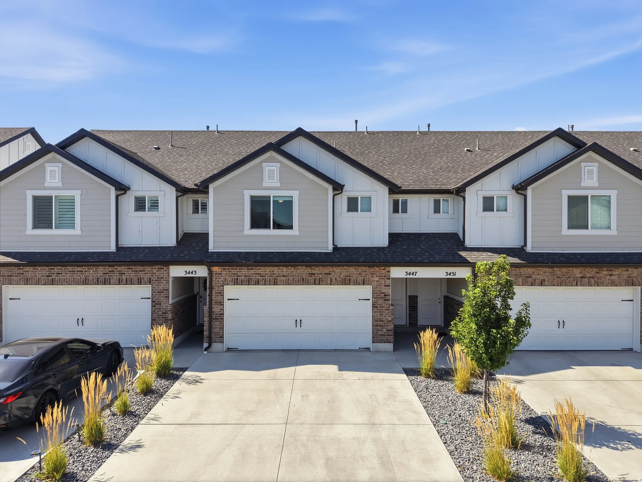Contemporary townhome exterior featuring light gray siding, dark shingle roofing, and a brick facade