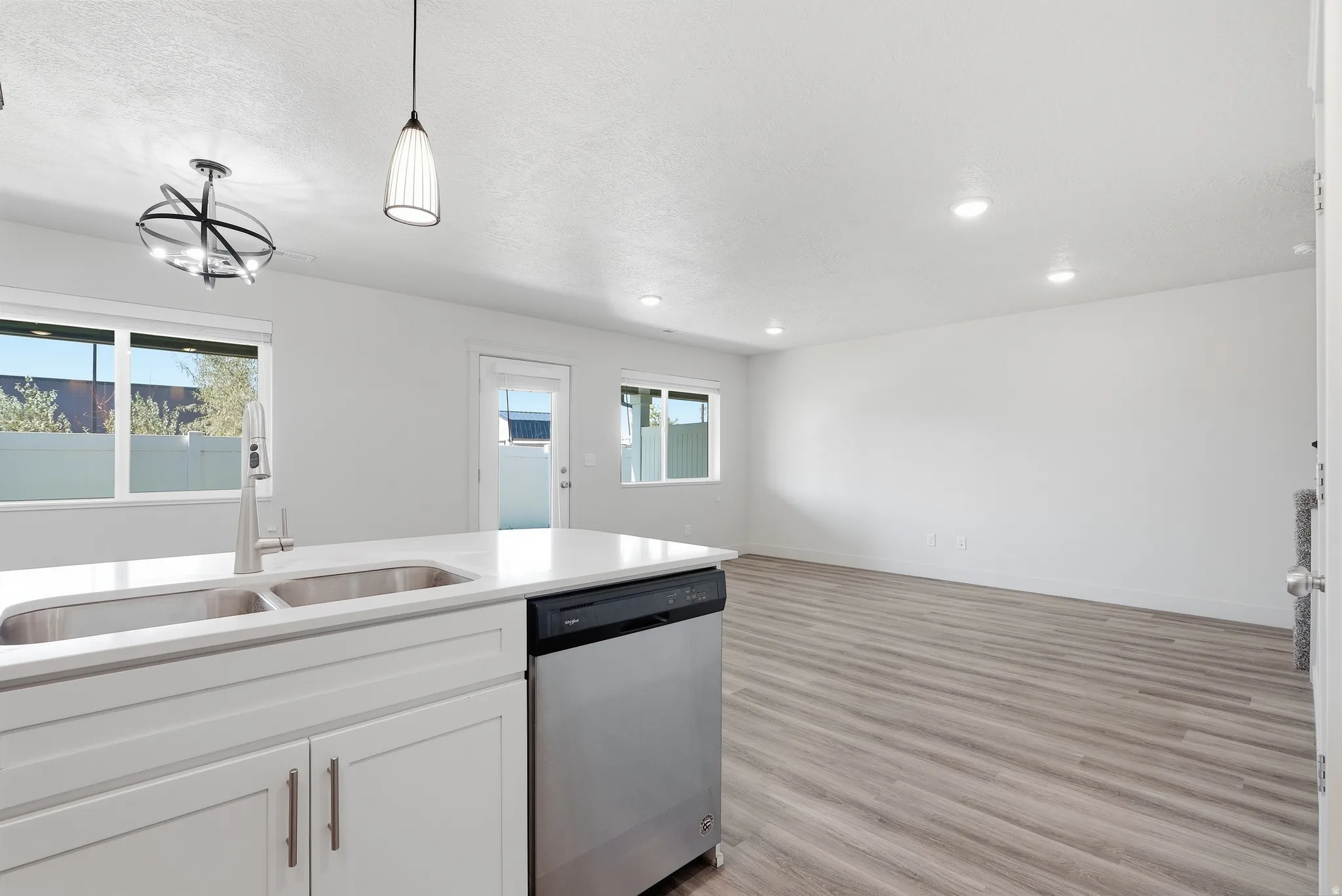 Kitchen island with double basin sink, white cabinetry, and stainless steel dishwasher