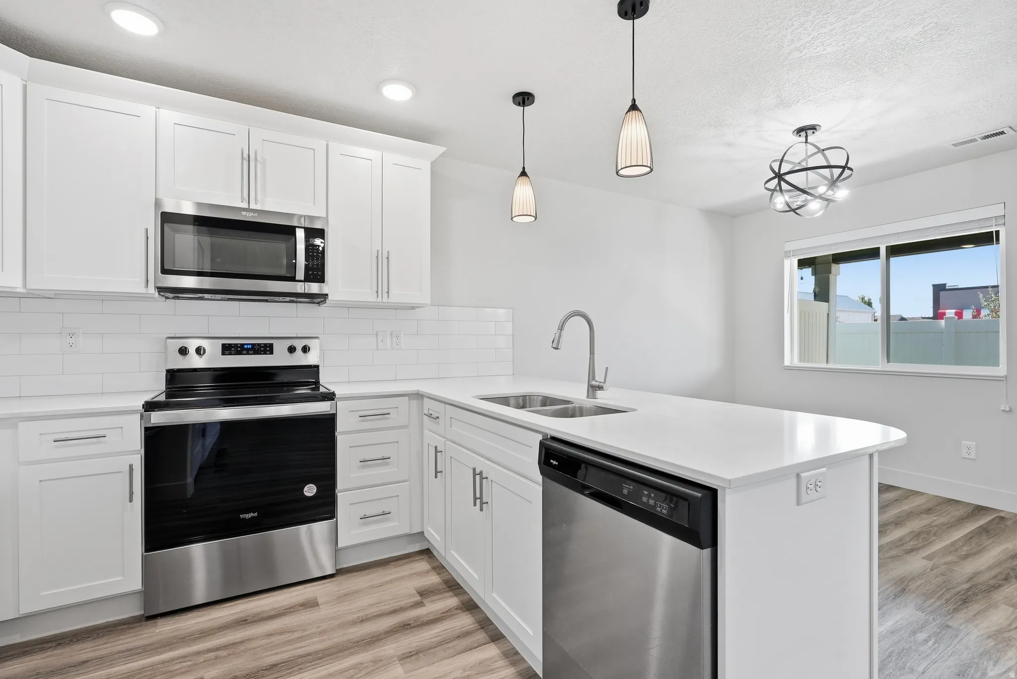 Bright kitchen featuring white cabinetry, stainless steel appliances, a center island with sink, contemporary pendant lighting, and wood-finish flooring