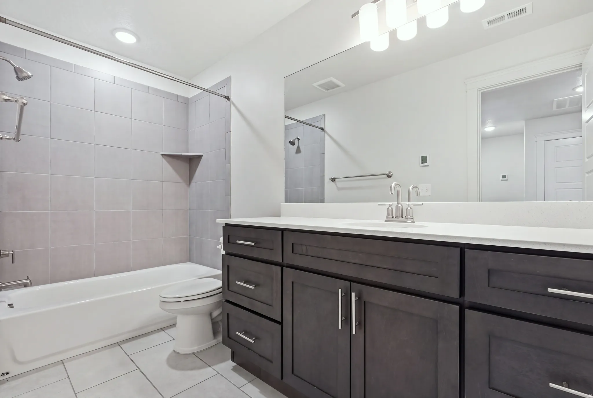 Bathroom featuring a tub/shower combination with light gray tile surround, built-in shower shelf, and a vanity with a white countertop and dark wood-finish cabinetry