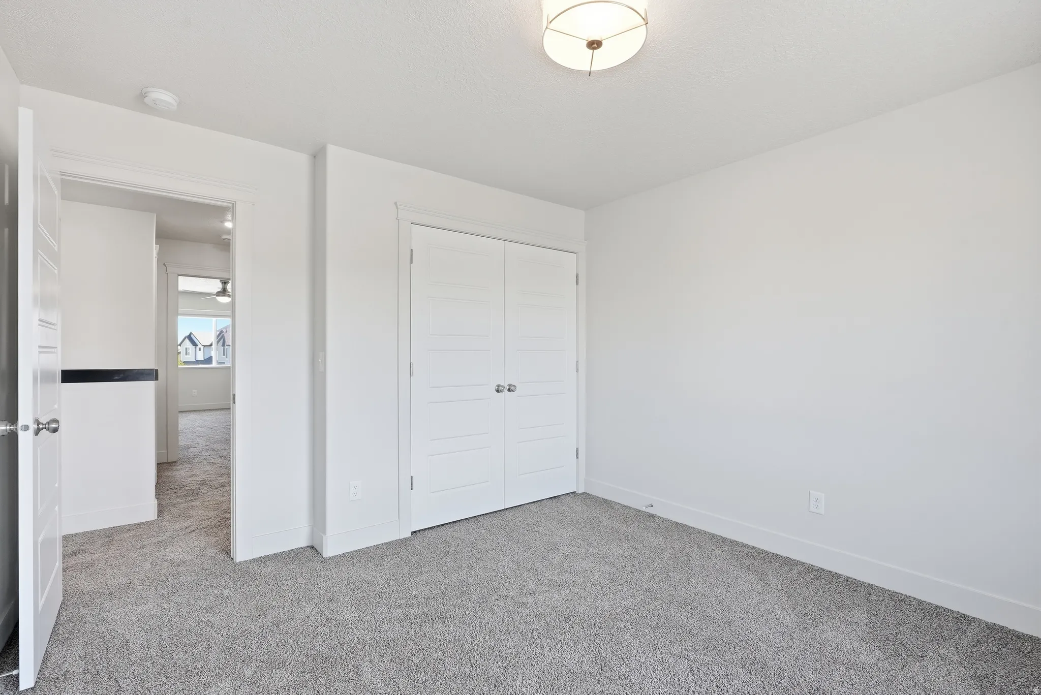 White interior walls, gray carpet flooring, white paneled doors, and a ceiling-mounted light fixture