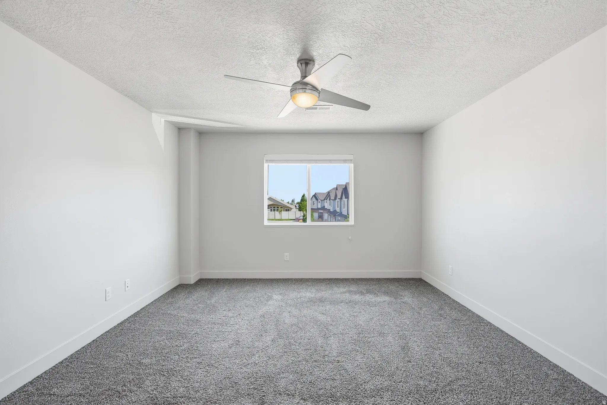 Neutral wall paint, textured ceiling, window with white trim, gray carpet, and a ceiling fan