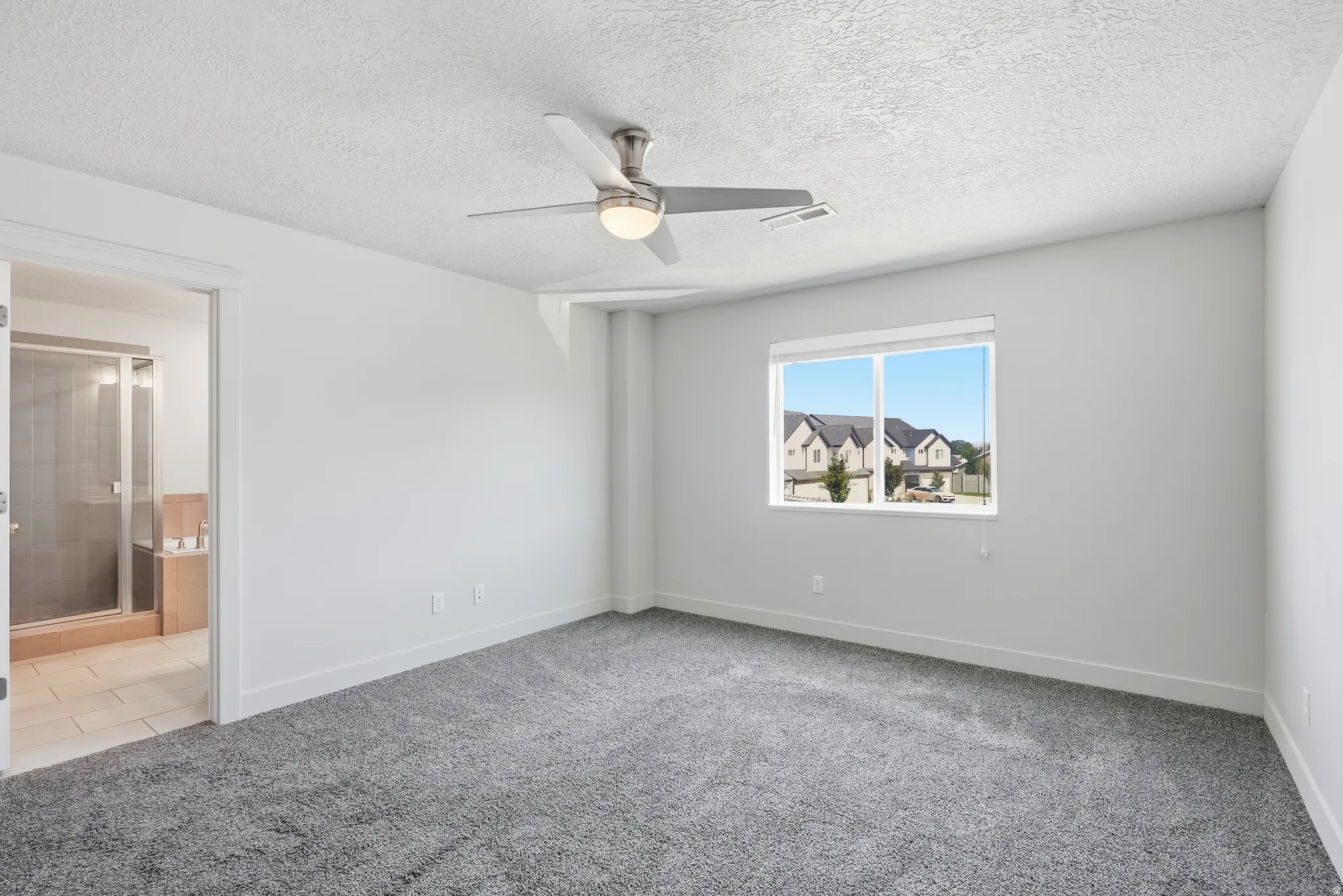 Spacious room featuring gray carpet flooring, white walls, a ceiling fan with integrated lighting, and a large window