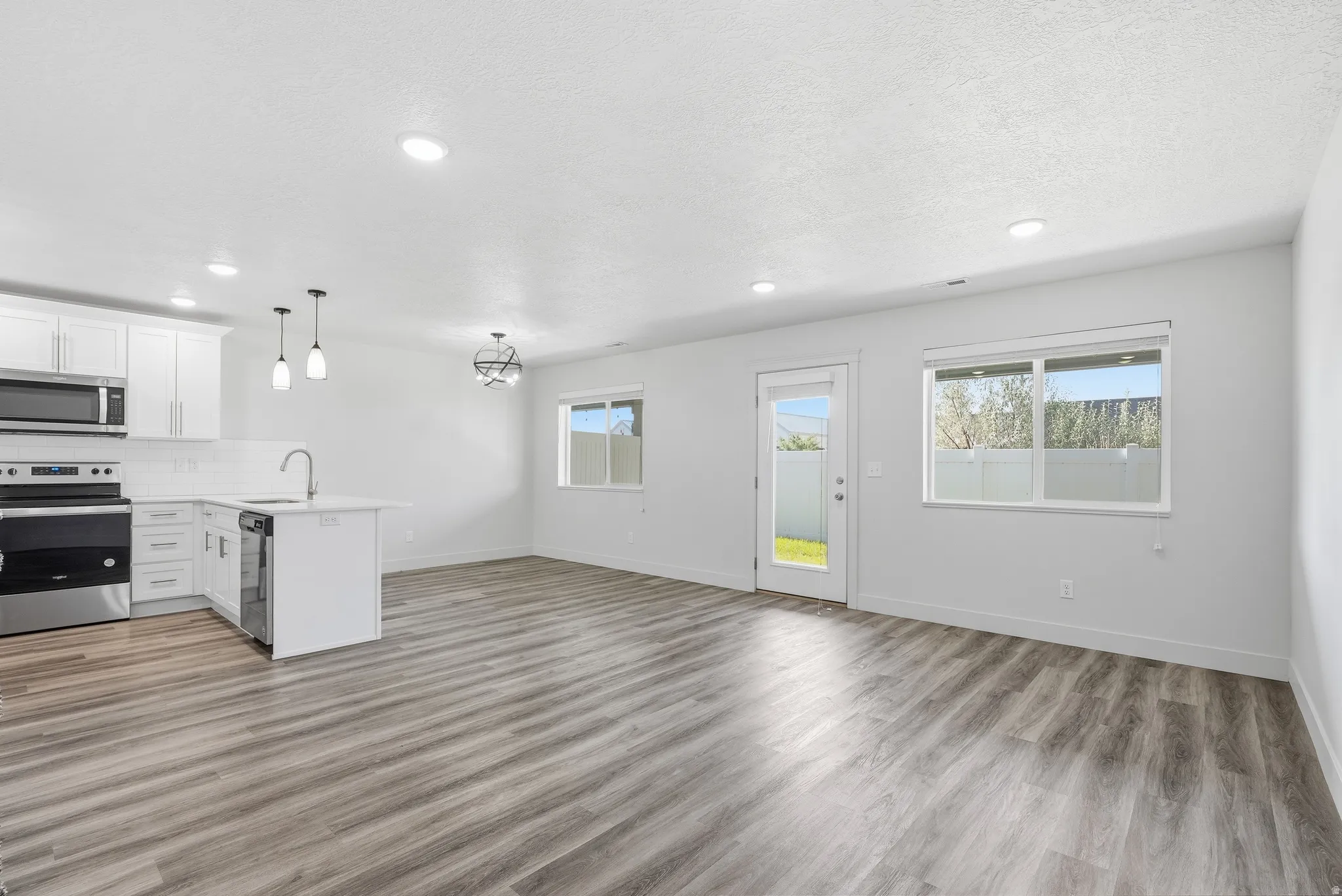 Open-concept living area featuring wood-finish flooring, white cabinetry, stainless steel appliances, and recessed lighting