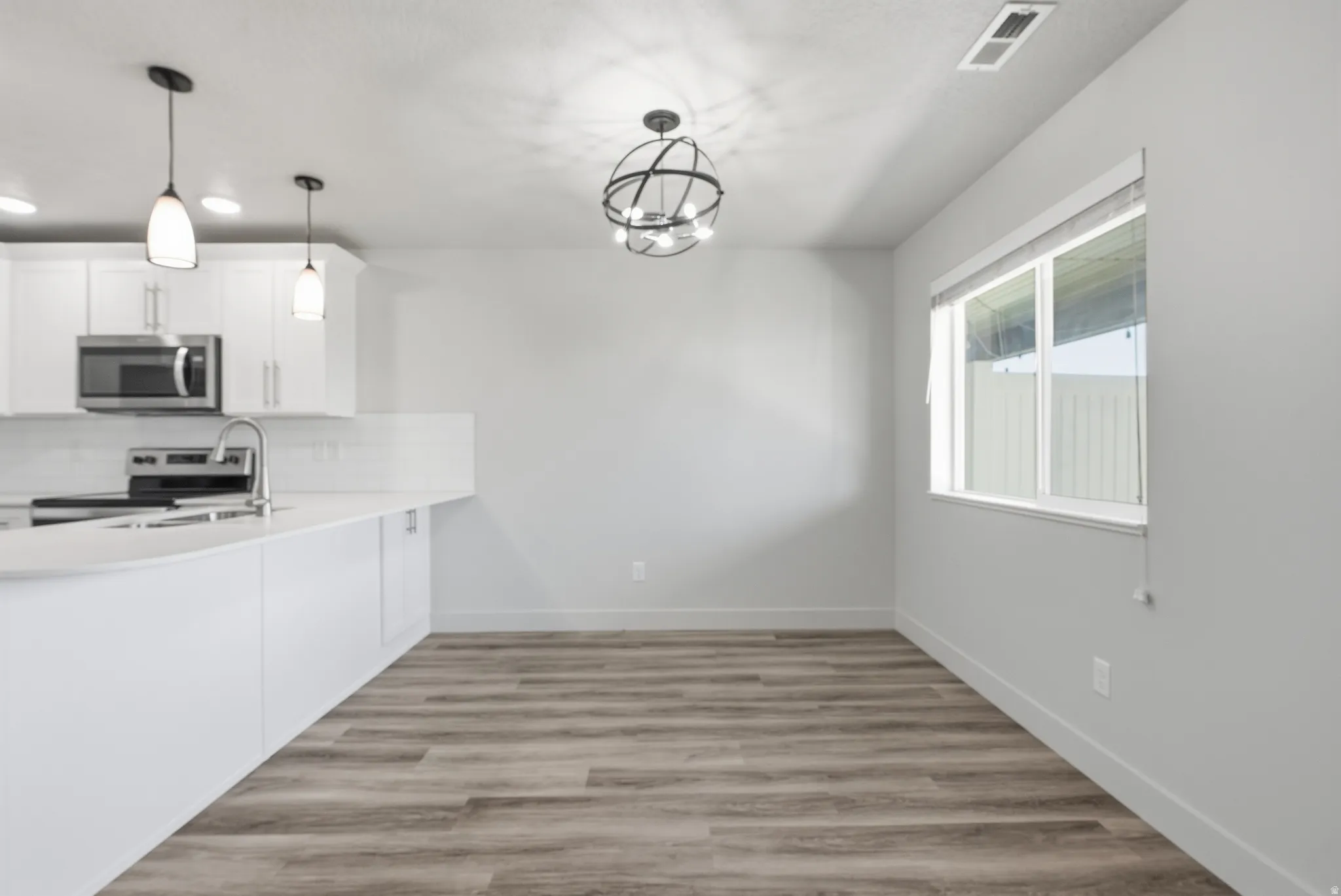White cabinetry with stainless steel appliances, pendant lighting, wood-finish flooring, and a large window