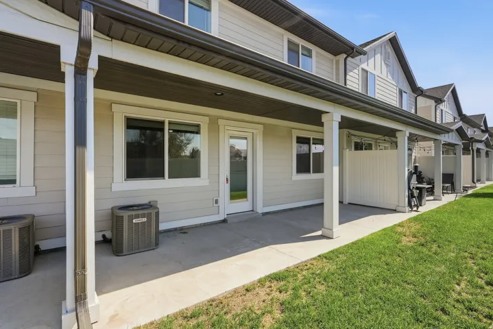 Covered concrete patio with white support columns, light-toned siding, and a manicured lawn
