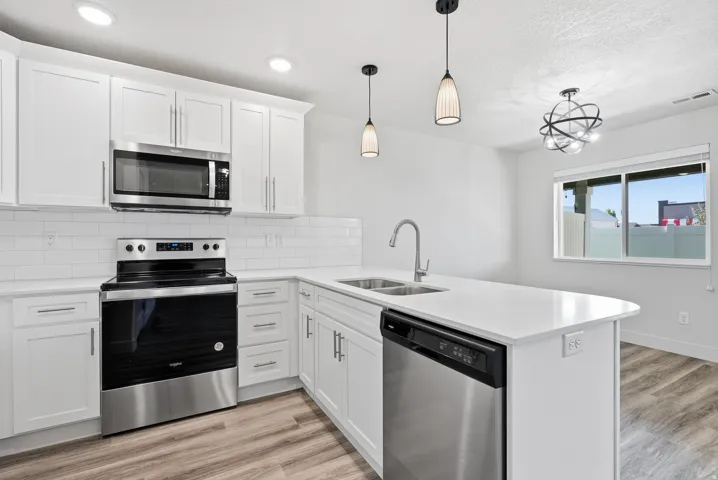 Bright kitchen featuring white cabinetry, stainless steel appliances, a center island with sink, contemporary pendant lighting, and wood-finish flooring