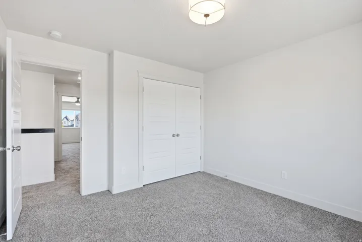 White interior walls, gray carpet flooring, white paneled doors, and a ceiling-mounted light fixture