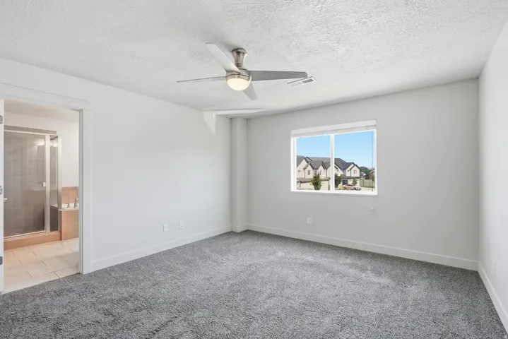 Spacious room featuring gray carpet flooring, white walls, a ceiling fan with integrated lighting, and a large window