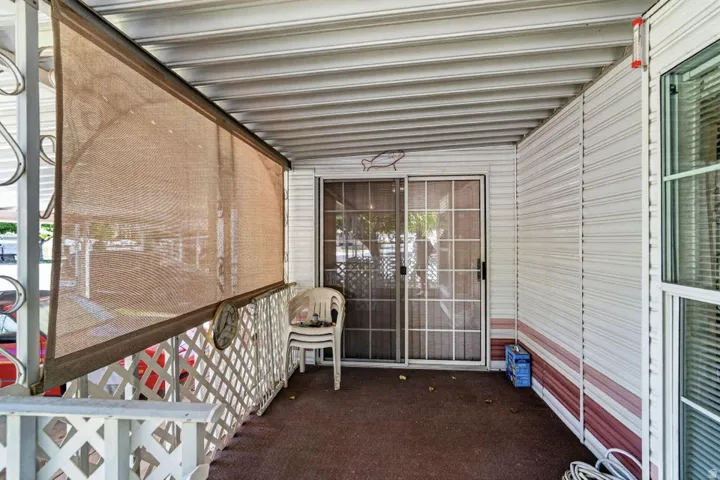 Covered patio with textured flooring, white lattice railing, and a pull-down screen shade