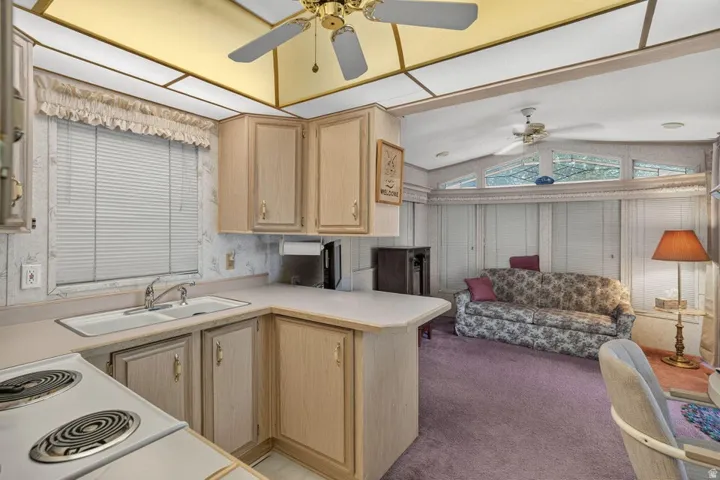 Kitchen area featuring light wood-finish cabinetry, a double basin sink with a chrome faucet, and a corner countertop