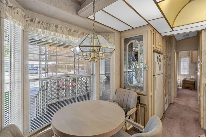 Bay window with horizontal blinds, built-in cabinetry with decorative glass panels, recessed ceiling lighting, and a brass-finish chandelier