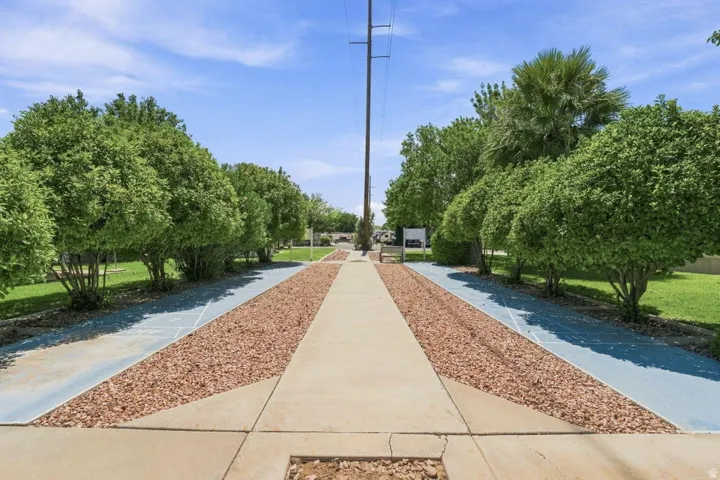 Concrete pathway with decorative gravel borders, flanked by mature trees and manicured lawns