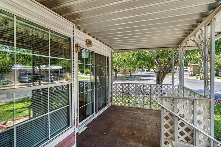 Covered porch with lattice railing, exterior light fixture, and sliding glass door