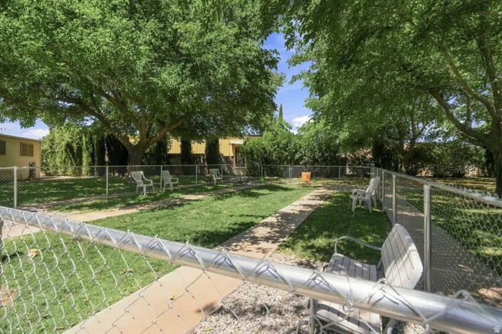 Fenced green space featuring mature trees and a concrete pathway