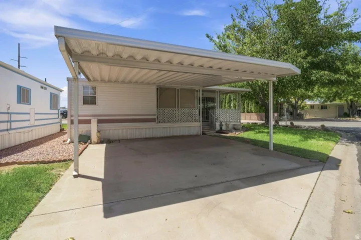 Attached carport with concrete driveway, screened-in porch with railing, exterior siding, and mature trees