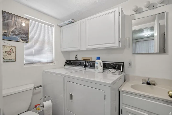 Integrated laundry appliances, white cabinetry with upper storage, built-in vanity with sink, wall-mounted mirror, and a window with blinds