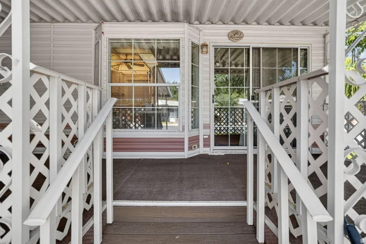 Covered porch with wood-finish decking, white lattice railings, multiple windows, and a sliding glass door