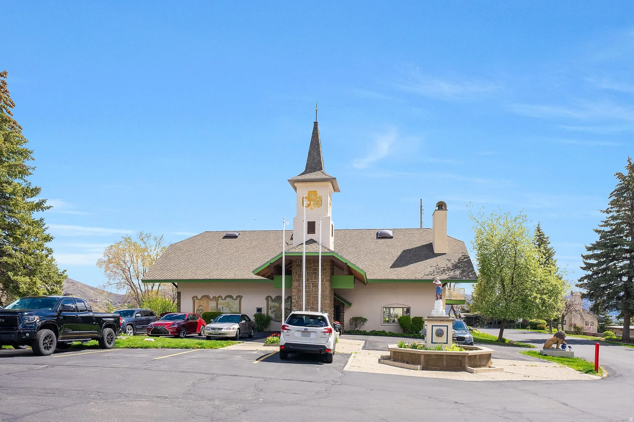 Stone-fronted building with a prominent steeple, multiple rooflines, and a paved parking area