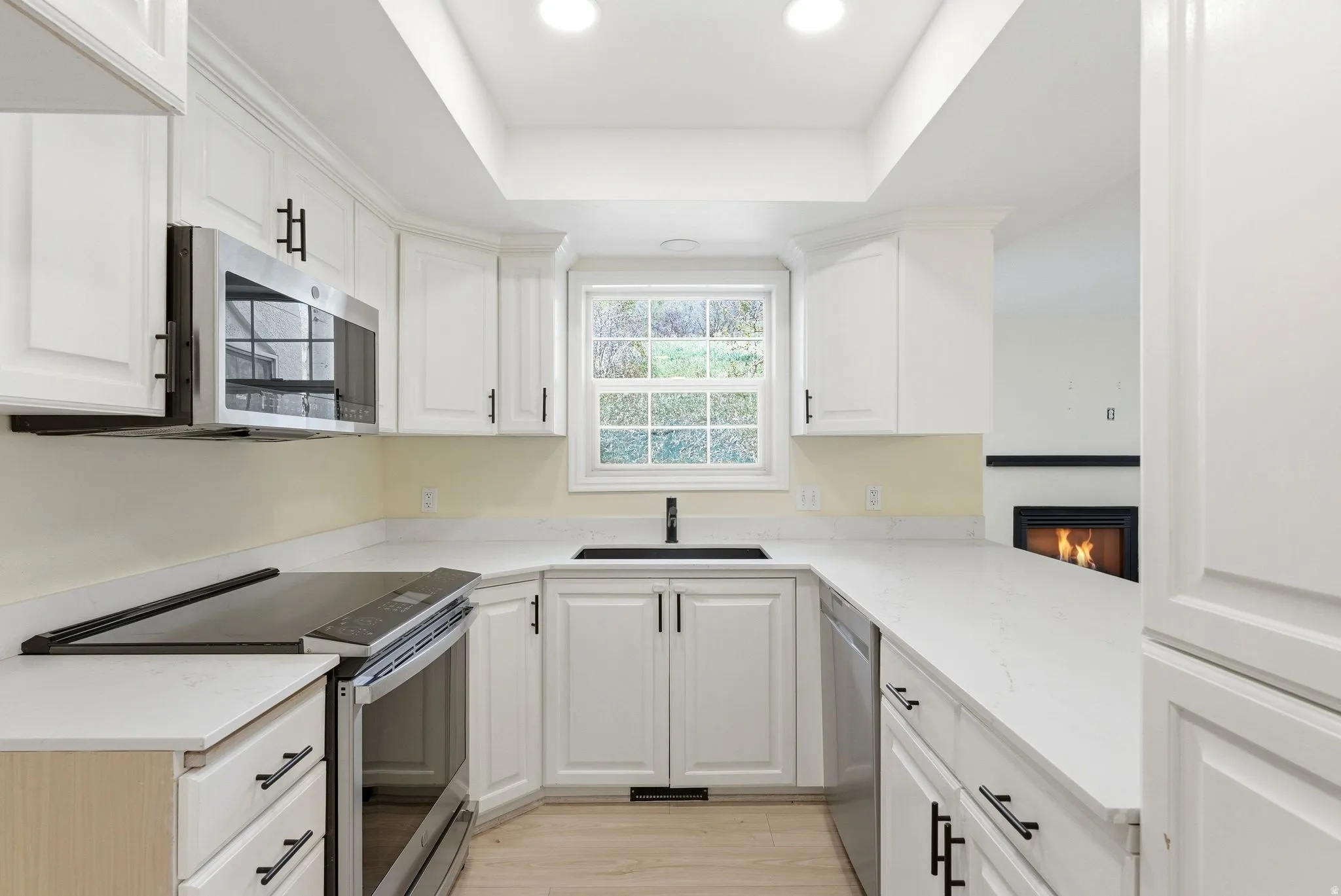 White kitchen featuring a U-shaped layout, white shaker-style cabinetry with matte black hardware, integrated stainless steel microwave, and a black sink with a matching faucet