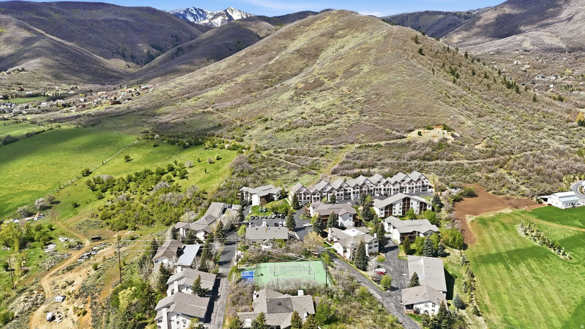 Aerial perspective featuring a residential community surrounded by expansive natural hillsides and distant snow-capped mountains