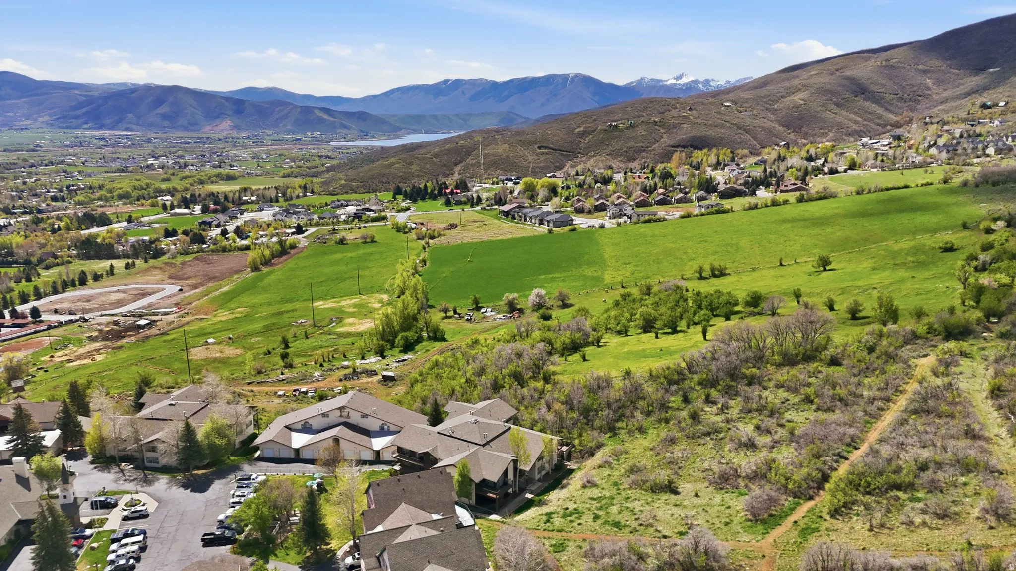 Expansive mountain landscape featuring varied terrain, a body of water, and residential structures amidst greenery