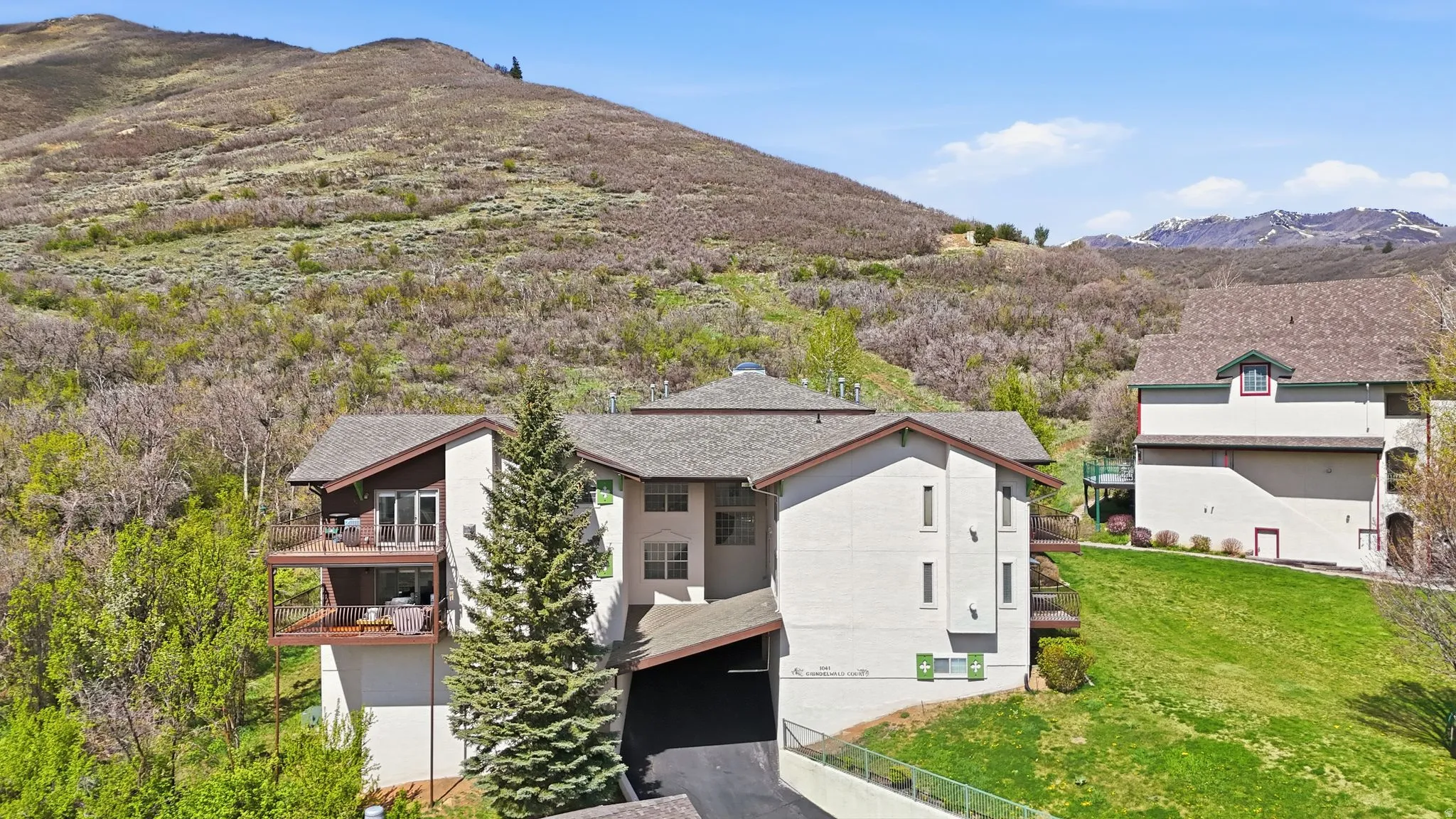 Multi-level structure with multiple balconies, covered parking, and a backdrop of a mountainous landscape