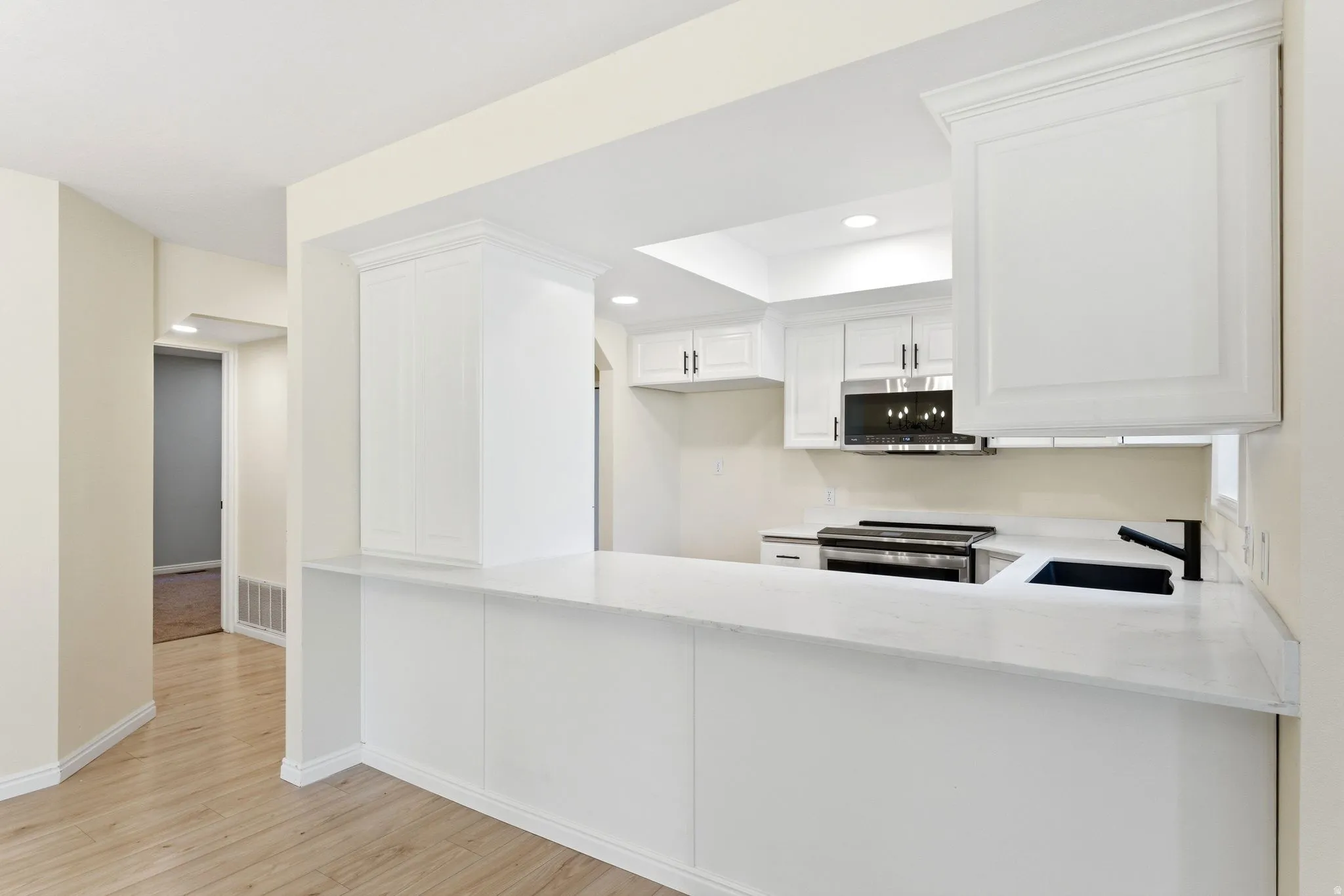 Kitchen featuring white cabinetry, light countertops, black kitchen sink, black faucet, and stainless steel appliances