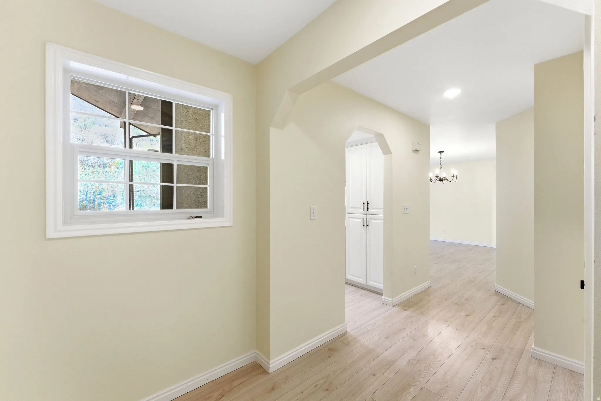 Interior hallway featuring light wood-finish flooring, an arched entryway, built-in white cabinetry, and white baseboards