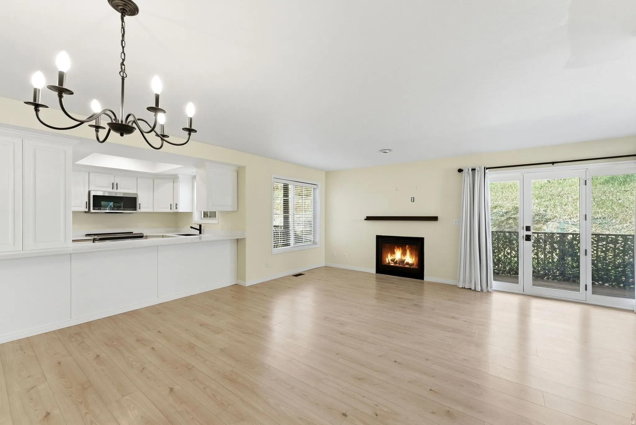 Open-concept living space featuring wood-finish flooring, a contemporary fireplace with a dark mantel, and a kitchen pass-through with white cabinetry