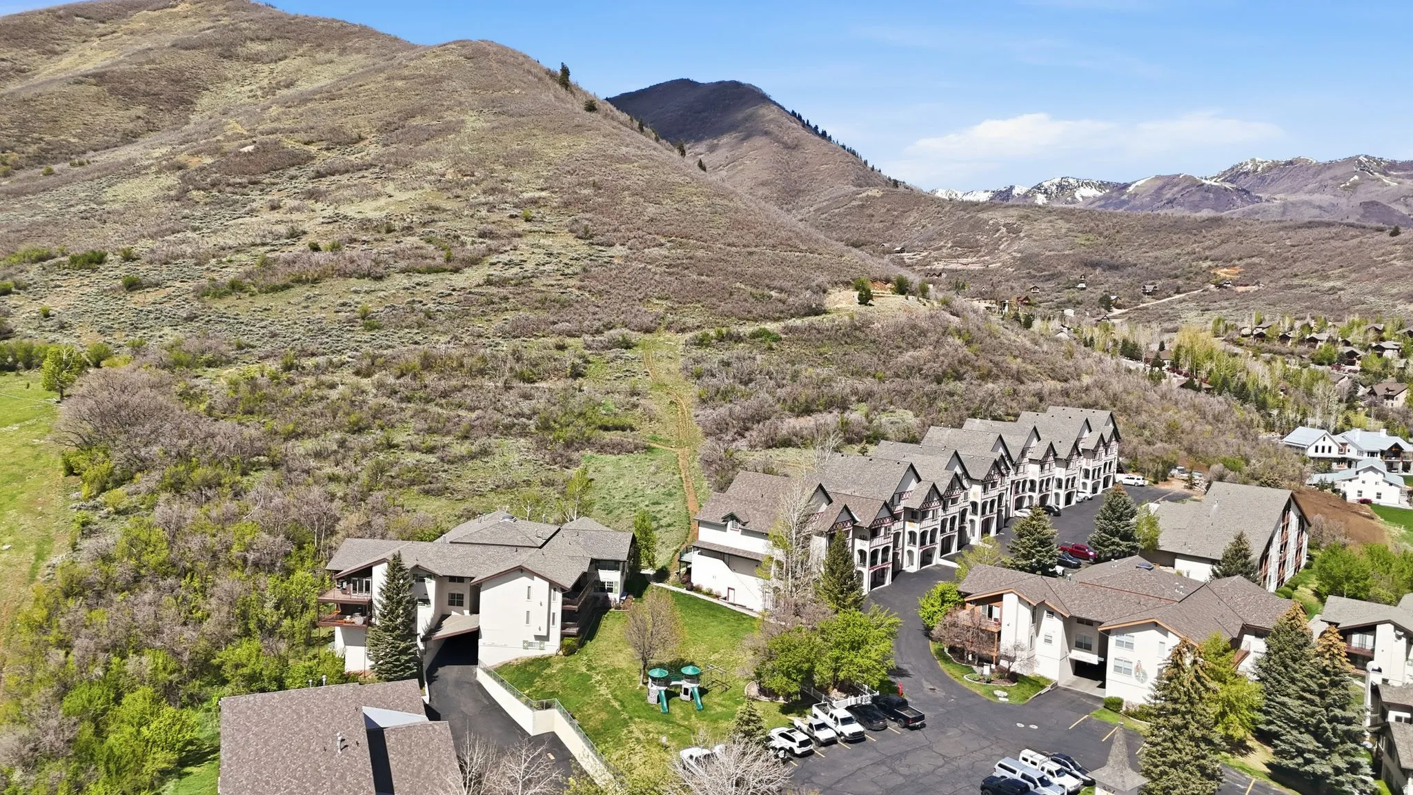 Expansive mountain landscape with a cluster of residential buildings featuring multiple rooflines, private balconies, and surrounding mature trees