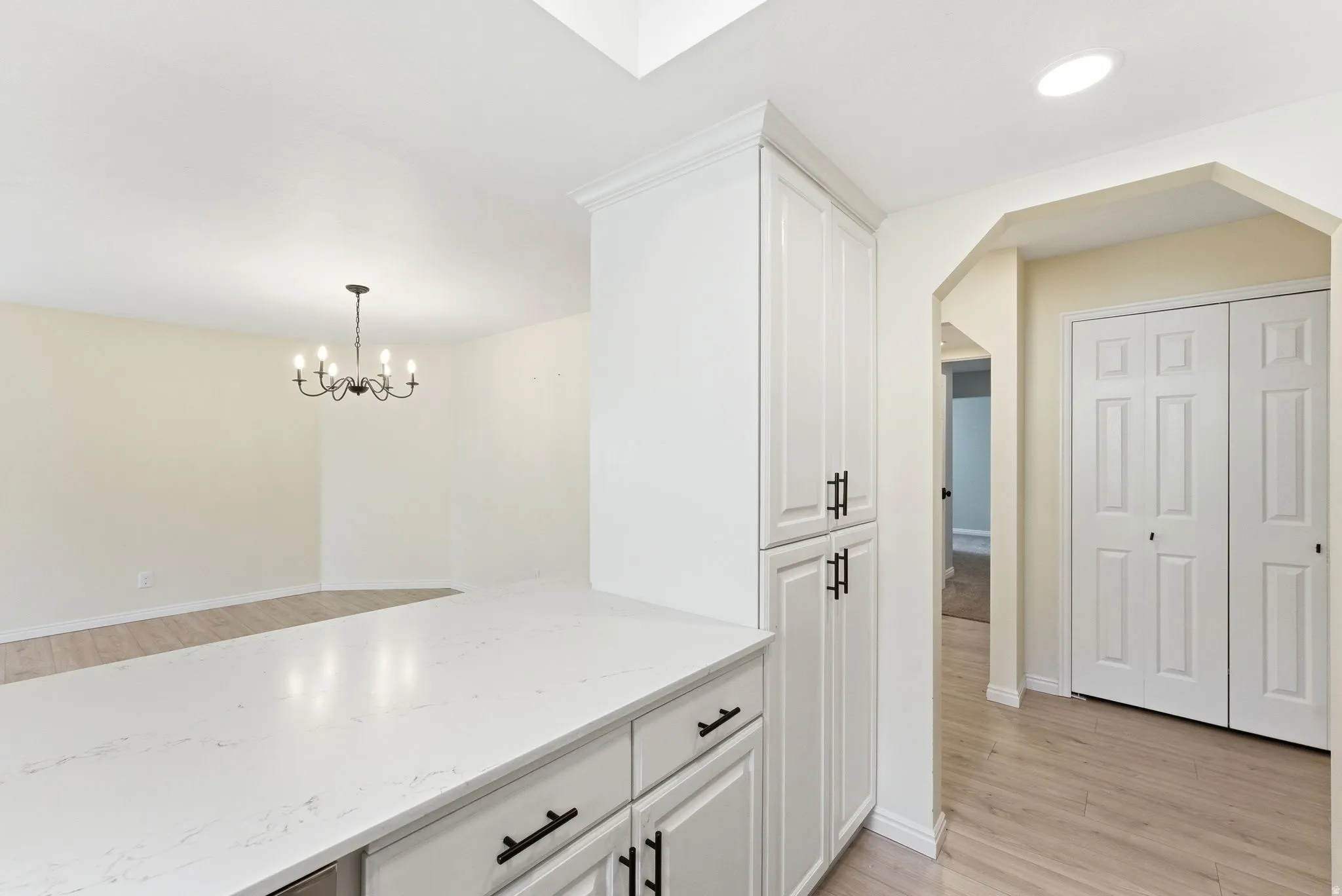 White cabinetry with black hardware, stone-finish countertops, wood-finish flooring, recessed lighting, and a suspended chandelier