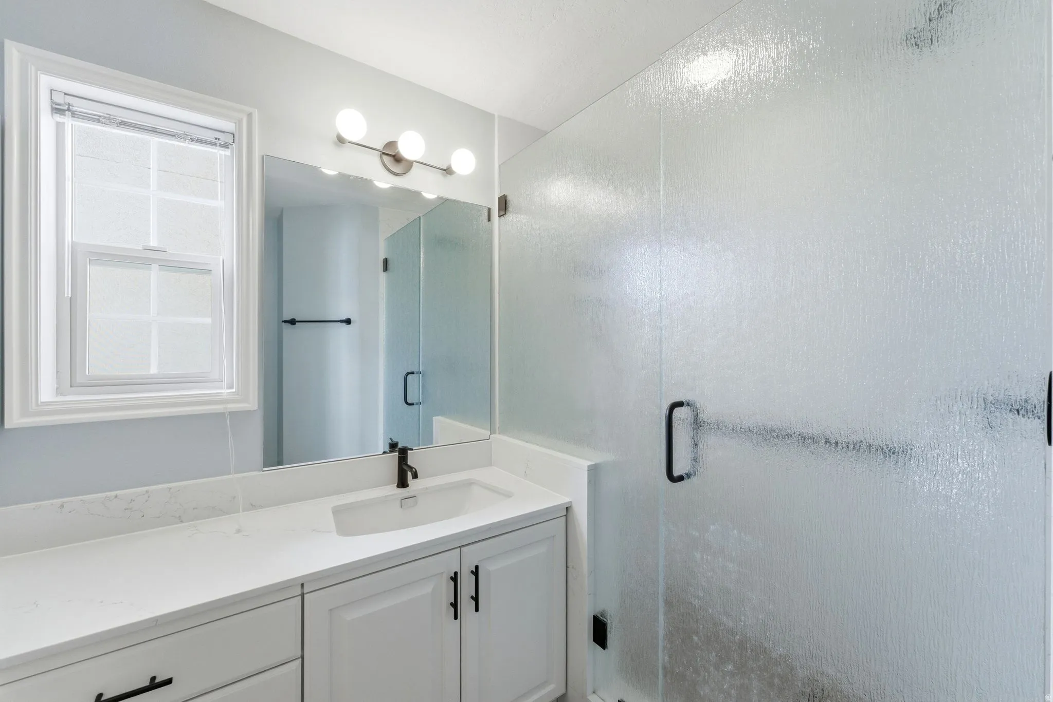 Bathroom featuring a frosted glass shower enclosure, white vanity with integrated sink, stone-finish countertop, and matte black fixtures