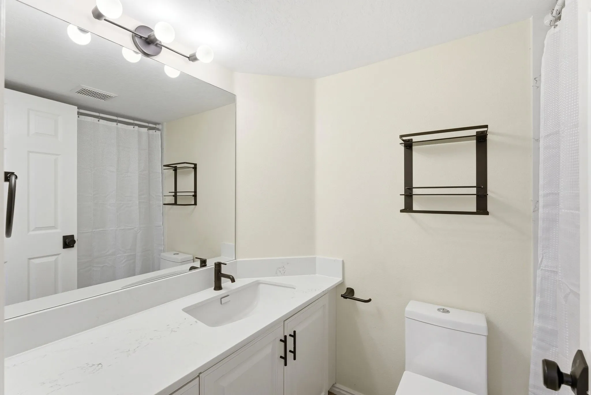 Bathroom featuring an integrated sink set into a white countertop, vanity with white shaker-style cabinetry and matte black hardware, and an elongated mirror