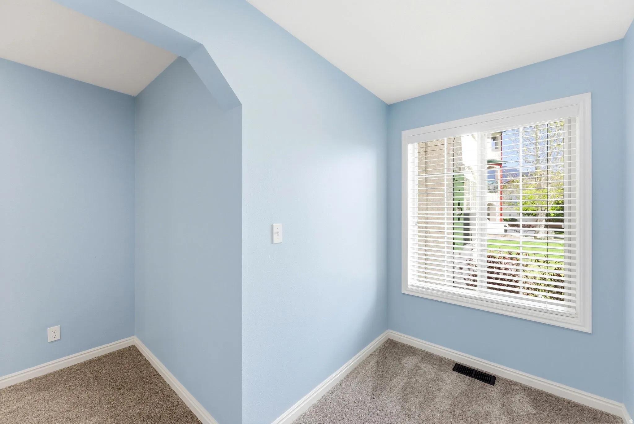 Light blue interior room featuring a large window with white blinds, white trim, and light grey carpet