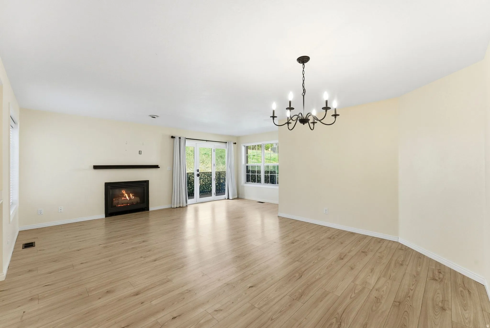 Spacious living area featuring wood-finish flooring, a fireplace with a black mantel, and a black chandelier