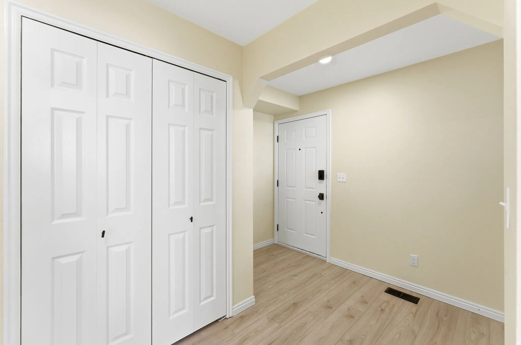 Entryway featuring a white paneled door, wood-finish flooring, and bi-fold closet doors with black hardware