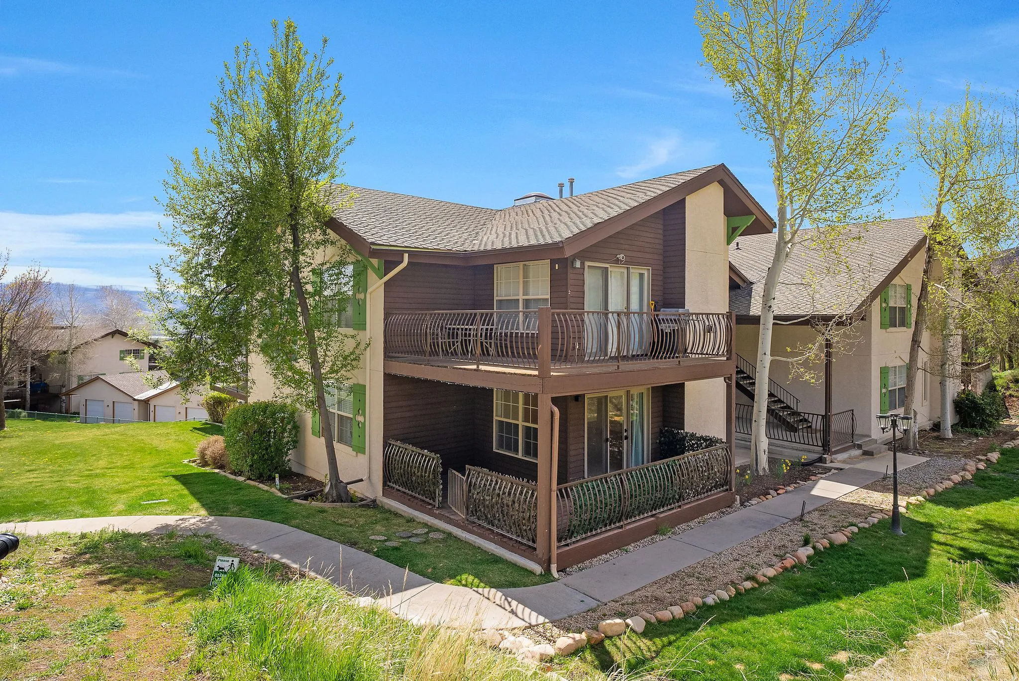Multi-story building featuring two private balconies with metal railings, a gabled roof, and a stucco facade with wood paneling accents