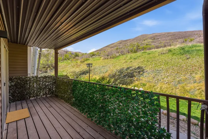 Covered outdoor balcony featuring wood-finish flooring, a metal railing, and a faux ivy privacy screen