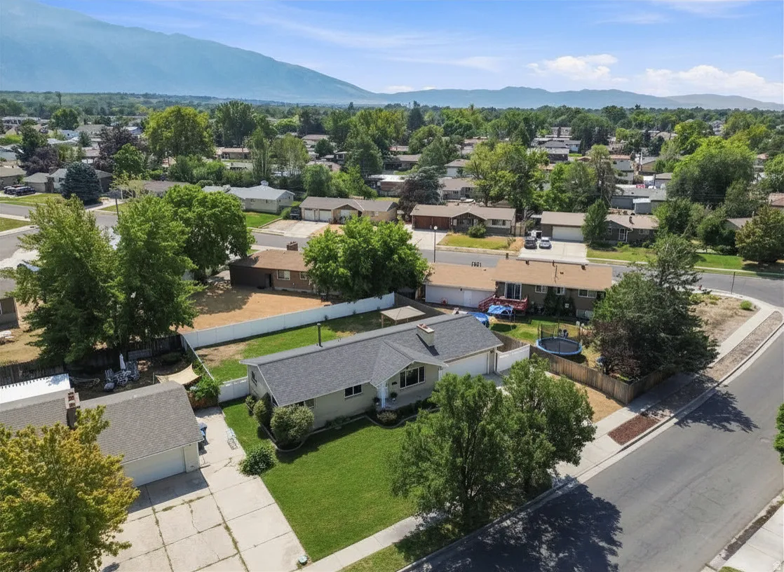 Single-story residence featuring an attached garage, manicured front lawn, and mature trees