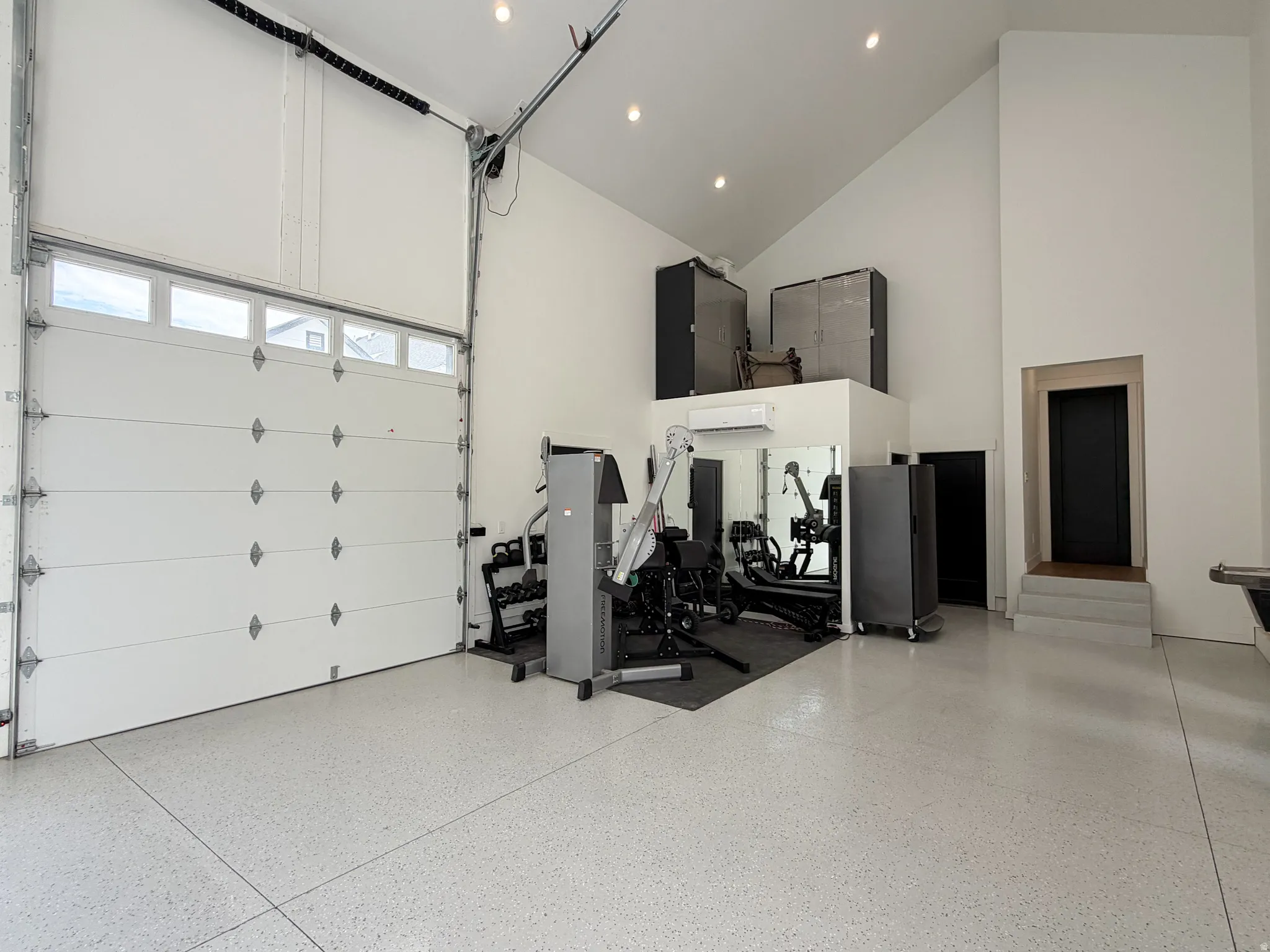 Vaulted ceiling, epoxy flooring, overhead garage door with upper window panels, and a built-in elevated platform