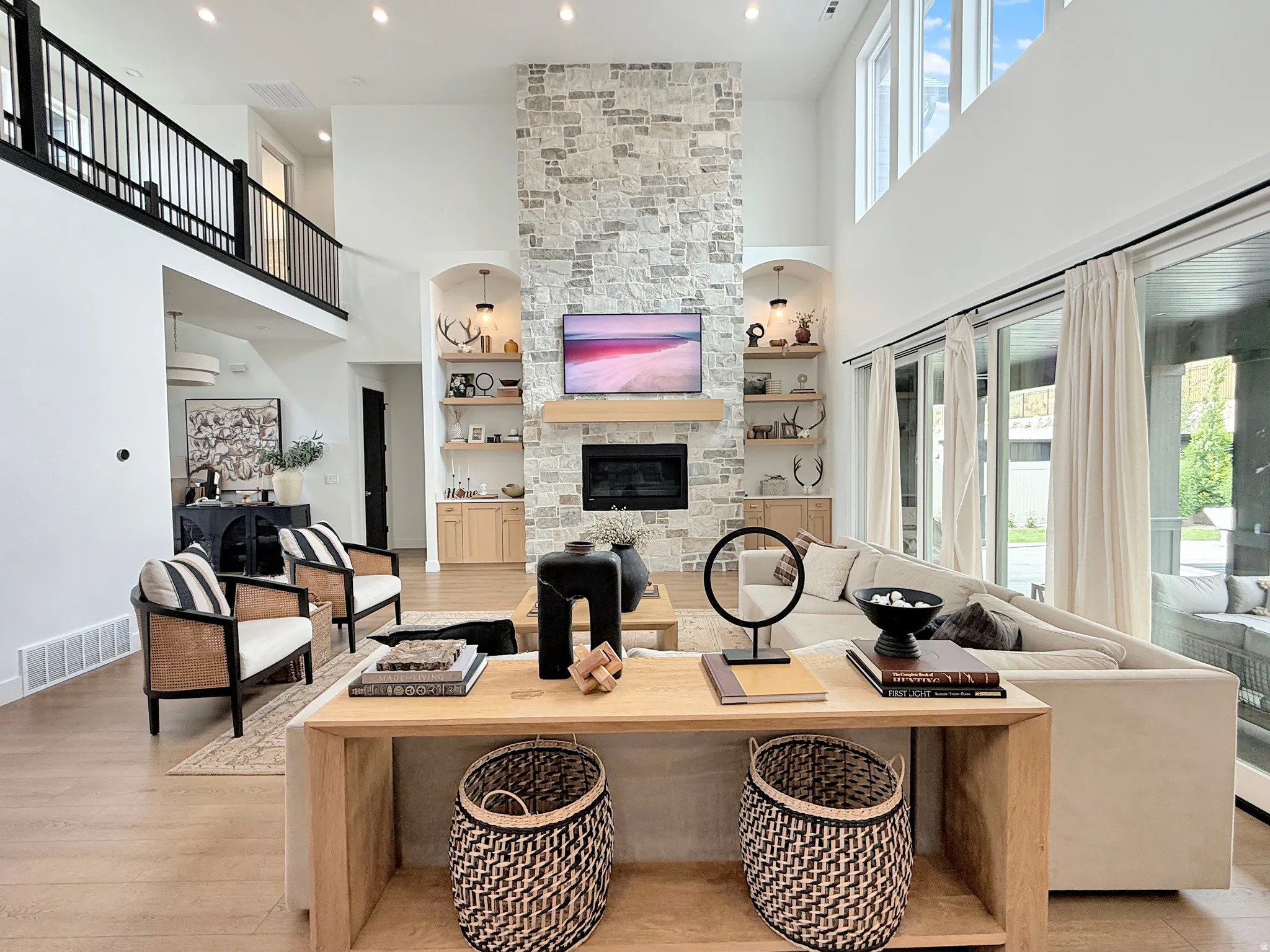 Two-story living area with a stone fireplace, wood-finish flooring, and a second-level open railing