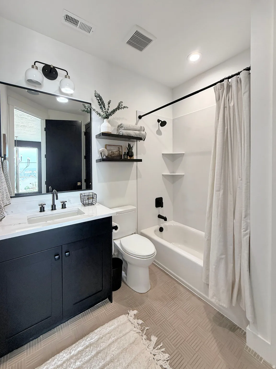 Modern bathroom featuring a black vanity with a white countertop and integrated sink, a full-size tub with a shower fixture, and light-toned patterned tile flooring