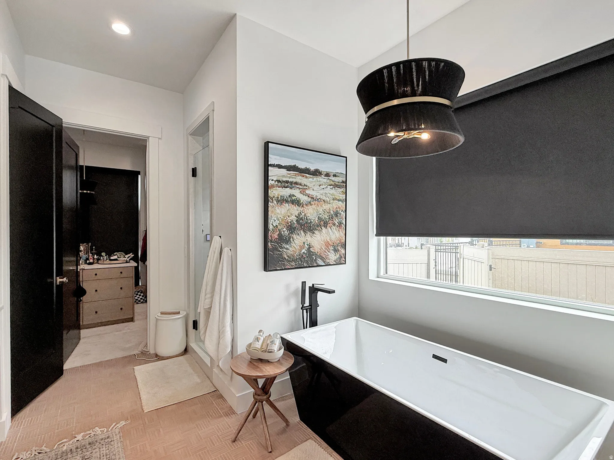 Freestanding soaking tub with matte black fixtures, an accent pendant light, and a window with roller shades