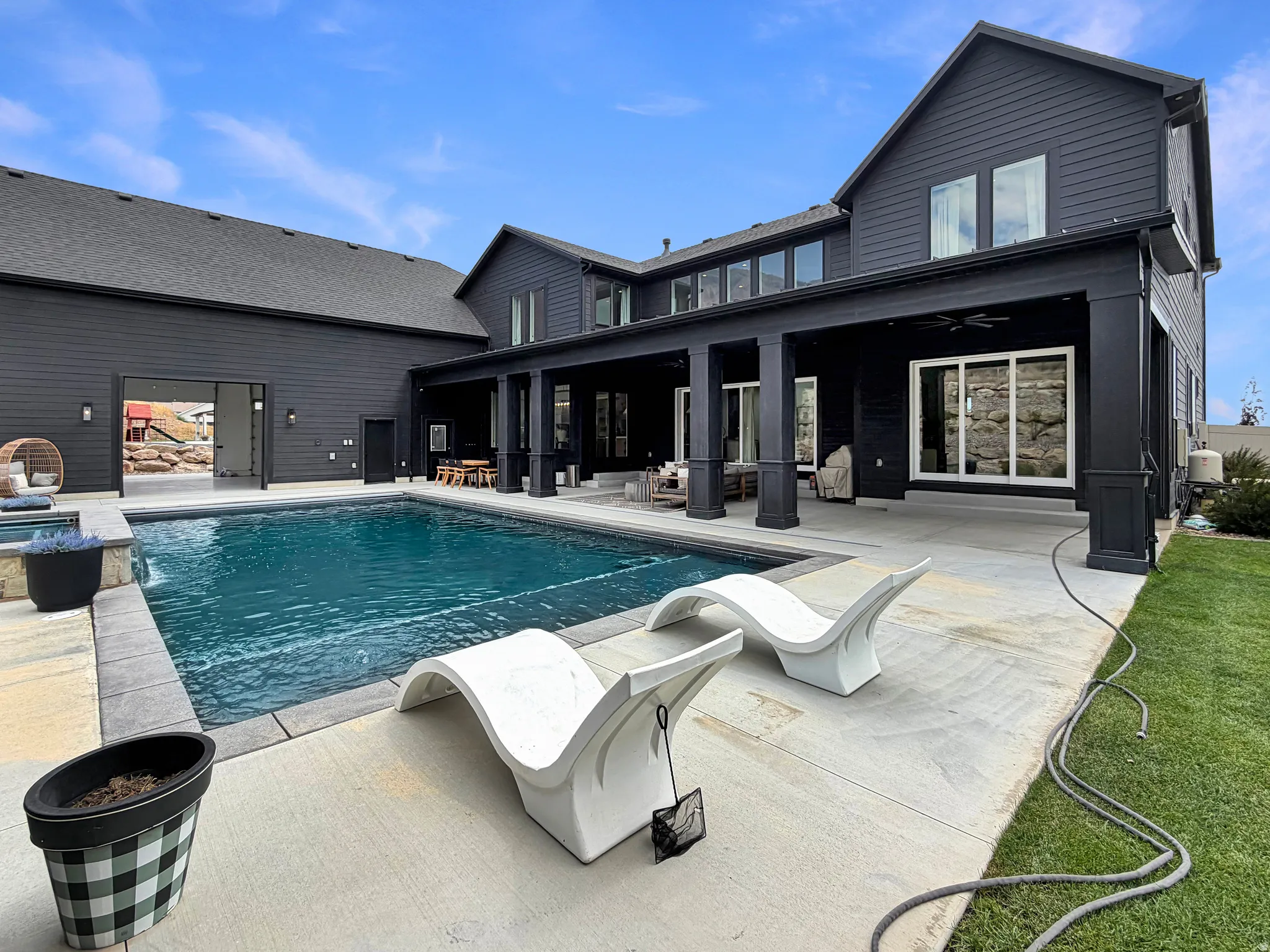 Expansive outdoor concrete patio featuring a built-in swimming pool and integrated hot tub, with a covered outdoor living area
