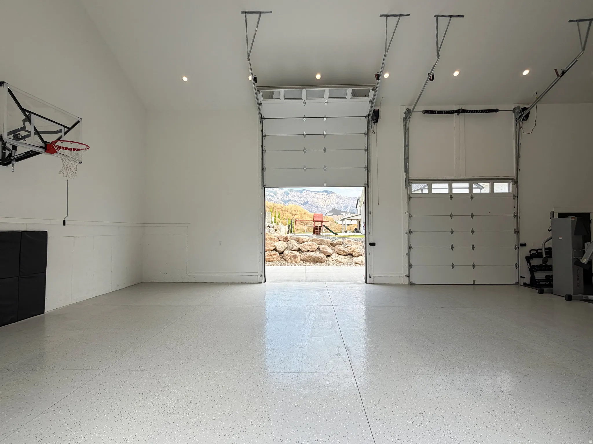 High-gloss epoxy flooring, multiple overhead garage doors, vaulted ceiling, recessed lighting, and white paneled walls
