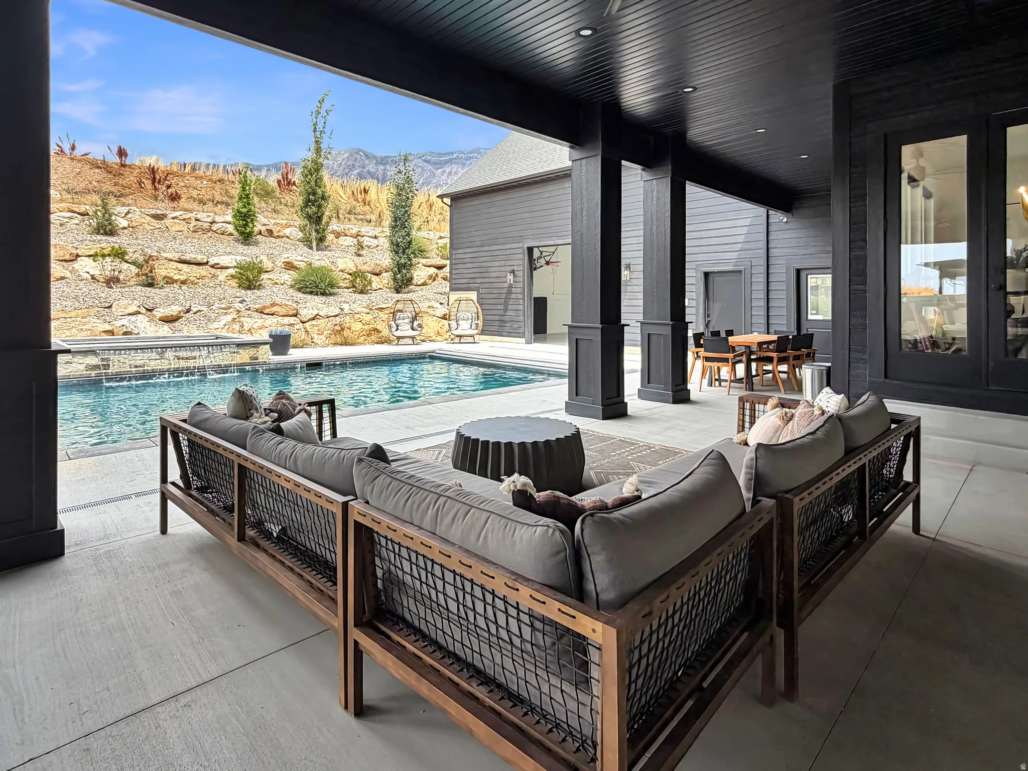 Covered outdoor patio with dark-stained wood ceiling and recessed lighting, leading to a concrete pool deck